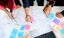 a group of people collaborating on a brainstorming session, with sticky notes, diagrams, and a laptop spread across a table.