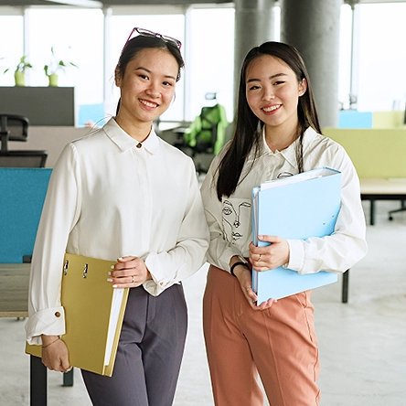 Two ladies holding folders smiling.